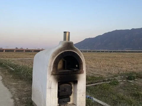 An oven at the edge of a rice paddy, a viaduct and a mountain behind